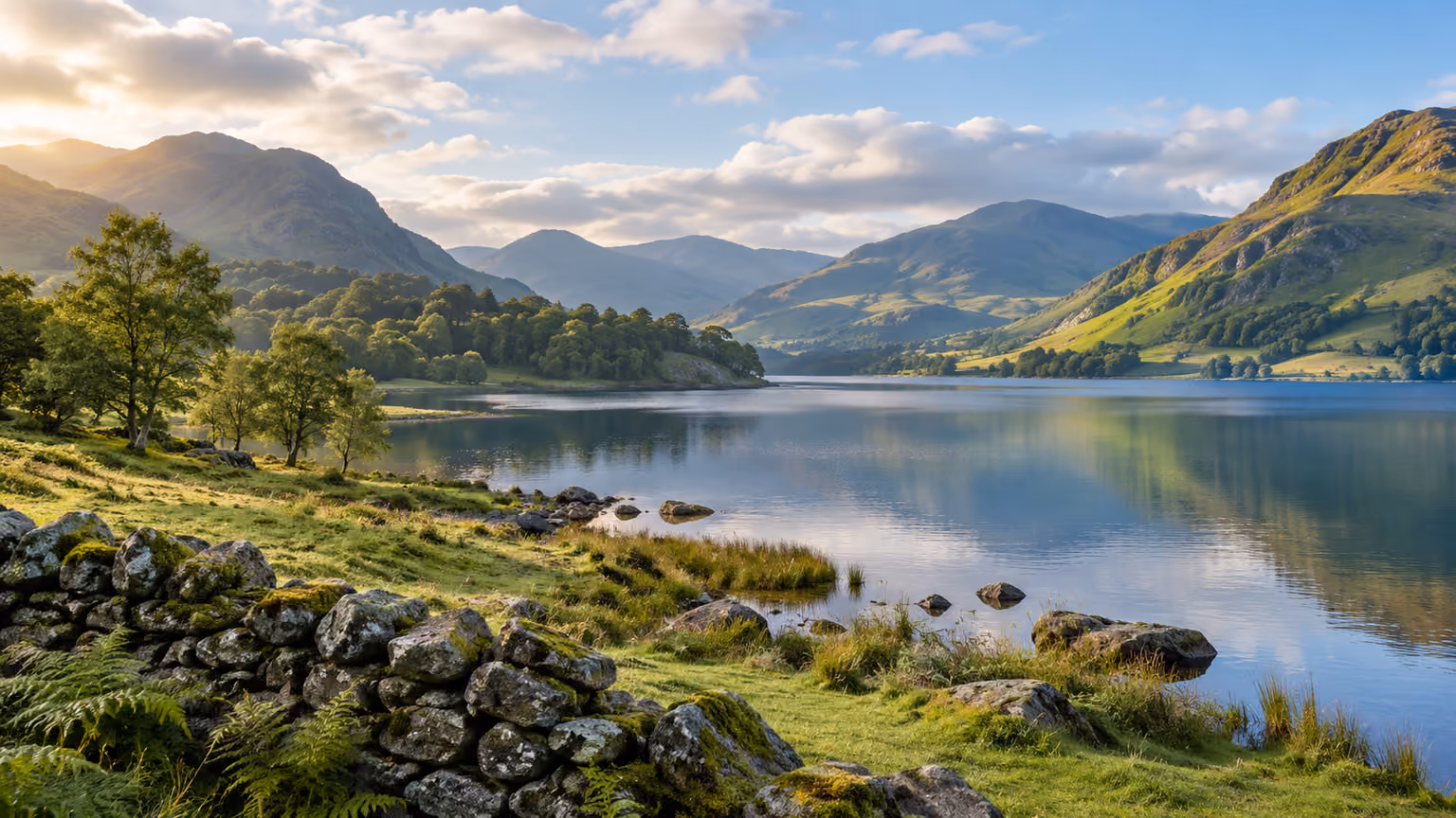 A blue lake and green hills beyond a stone wall in a Lake District landscape