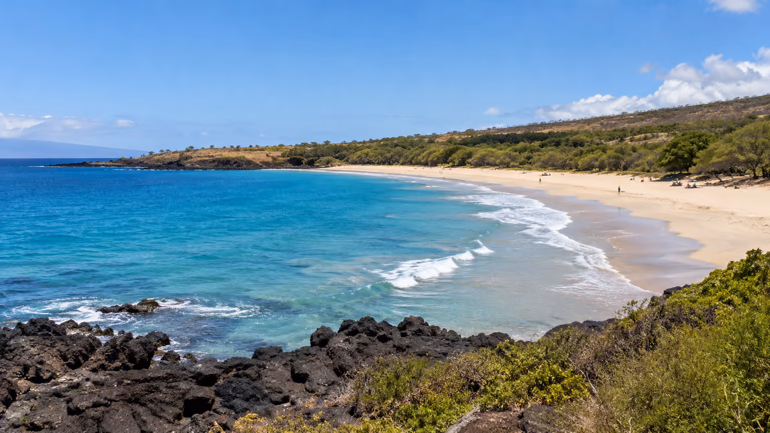 White sand and blue Pacific surf between low volcanic rocks on Hawaii’s Big Island