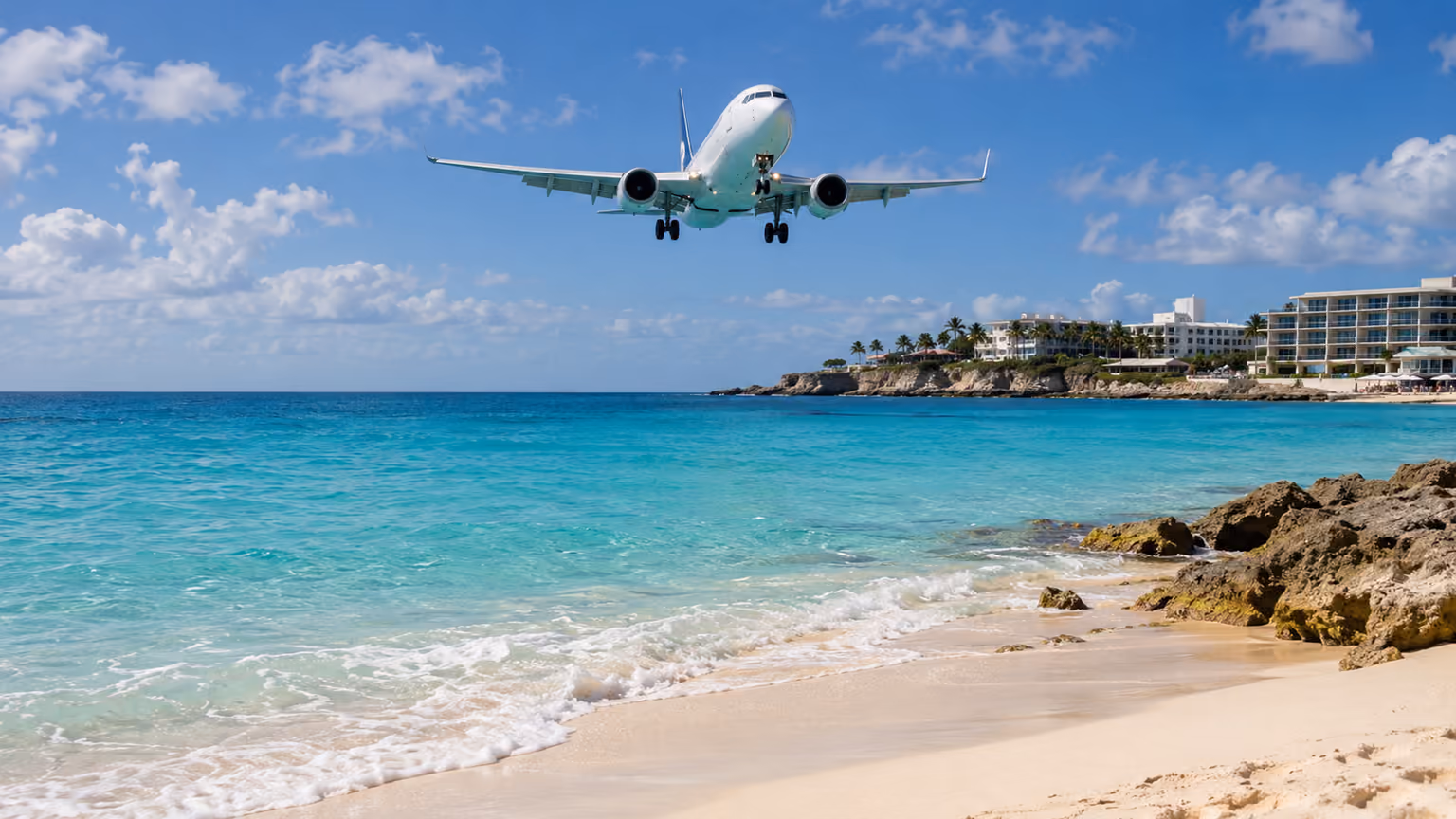 An unbranded passenger aircraft approaching above turquoise water beside Maho Beach